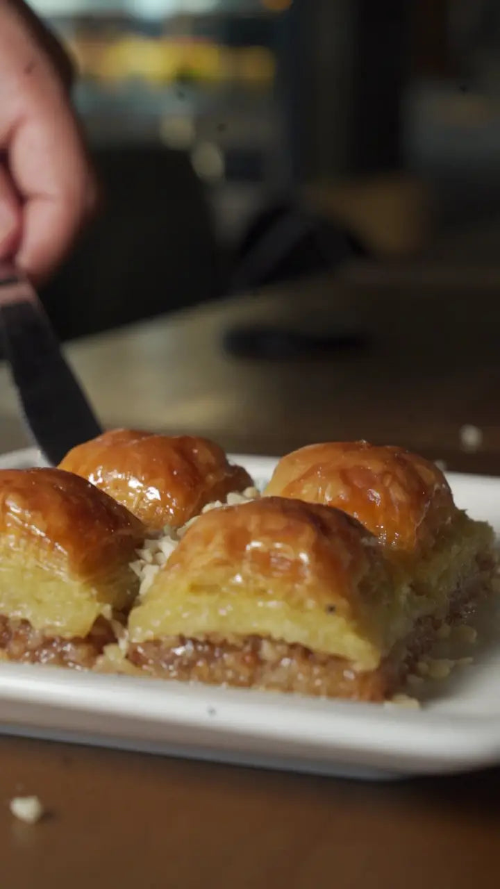 Ein Stück Baklava wird mit einem Heber vom Teller gehoben, die Teigschichten sind zu sehen